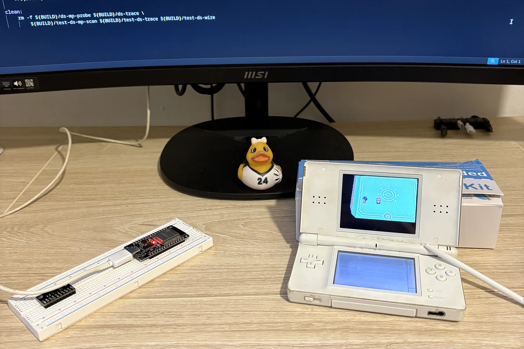 Workbench with a Nintendo DS displaying the Pokémon Platinum Union Room, an ESP32 on a breadboard, and protocol code on the monitor.